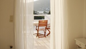 Un dormitorio con cama, una silla y vistas a un balcón con una silla.