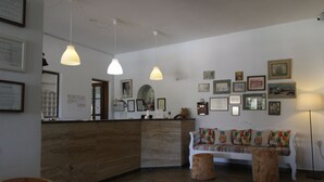 Un área de recepción con un mostrador de madera, un sofá blanco con cojines de colores y varias fotografías enmarcadas en la pared.