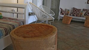 Una habitación con una cama, una silla blanca, un taburete de madera, un sofá y suelo de baldosas.