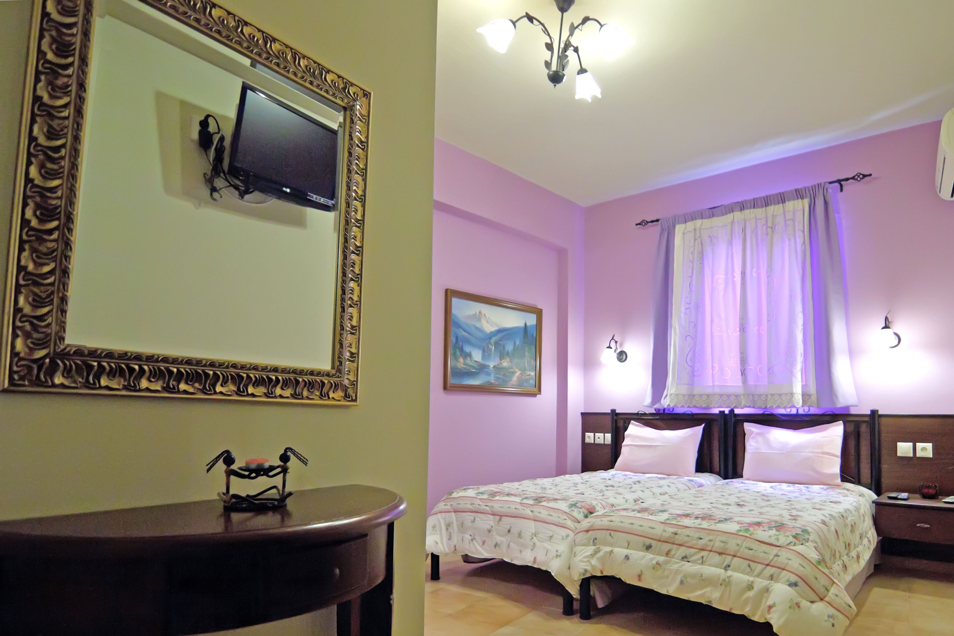 A bedroom with a bed, a TV mounted on the wall, a nightstand, a lamp, and a painting on the wall.
