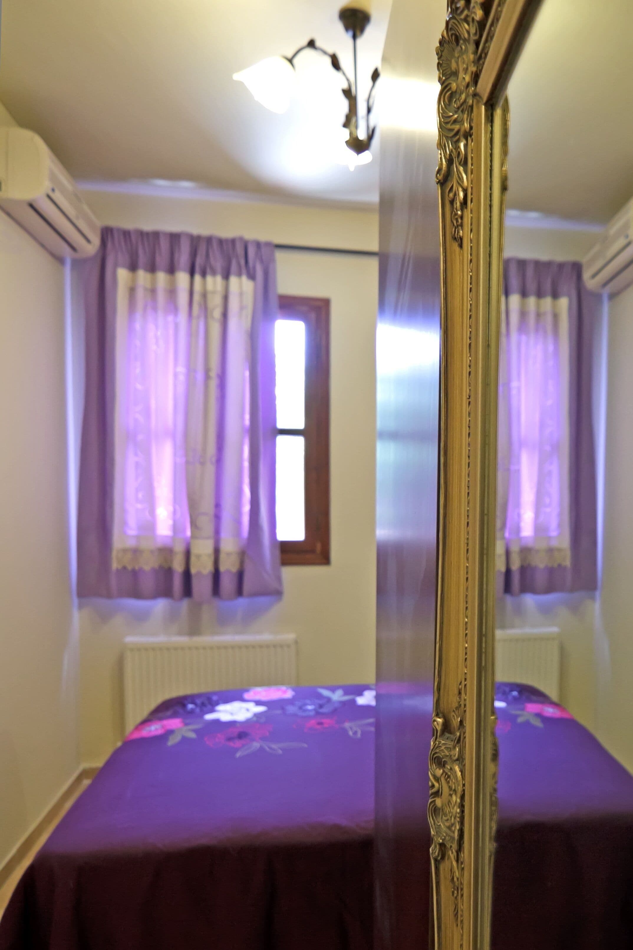 A bedroom with a large mirror, purple curtains, a floral bedspread, and a ceiling light.