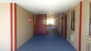 A narrow hallway with a blue carpet, red-framed windows, and a fire exit sign. - Budget Inn (Bartlesville)