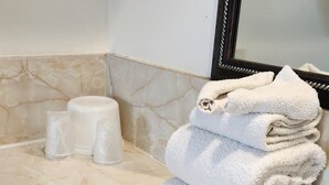 A bathroom with a marble floor, a stack of white towels, and two clear plastic bottles. - Budget Inn (Bartlesville)