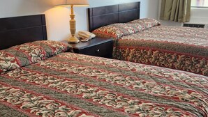 A hotel room with two beds, each with floral-patterned bedding, a bedside lamp, and a telephone on the nightstand. - Budget Inn (Bartlesville)
