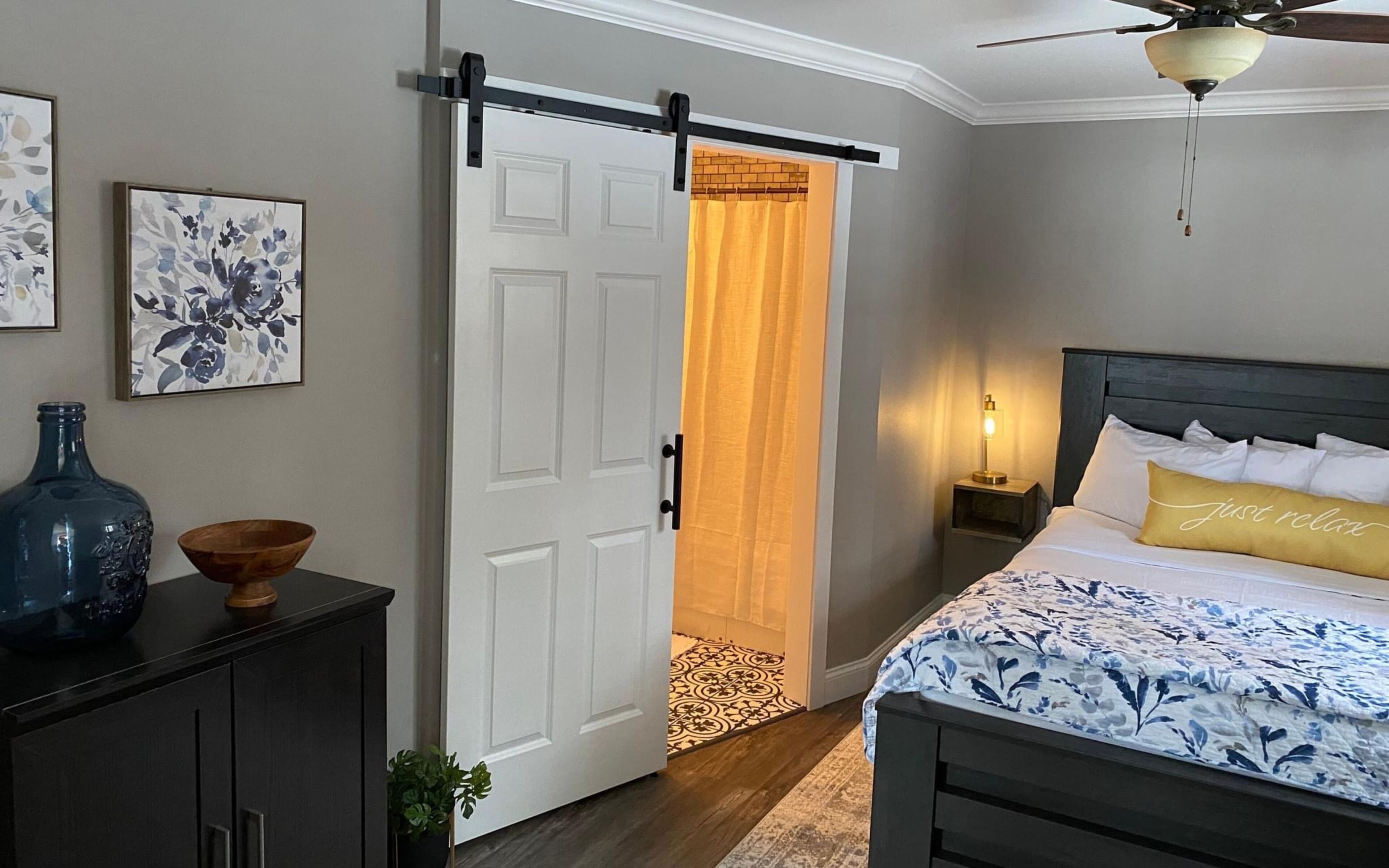 A bedroom with a bed, a nightstand, a wall-mounted lamp, a ceiling fan, and a sliding door leading to a bathroom.