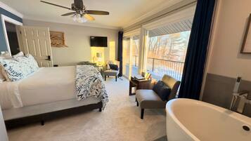 Habitación de hotel con cama, una zona de estar con una silla y una mesa, una bañera grande y un ventilador de techo.