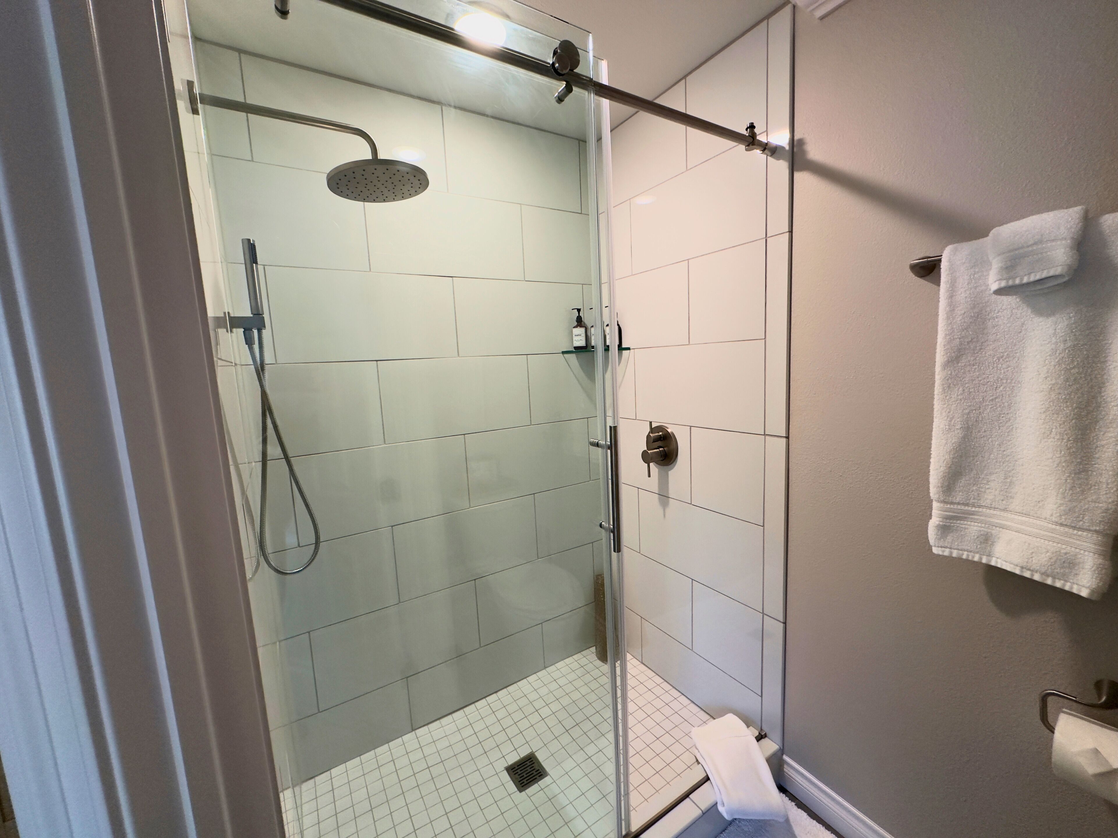 A glass-enclosed shower with a handheld showerhead, a glass door, and a towel rack with a folded towel.