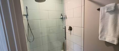 A glass-enclosed shower with a handheld showerhead, a glass door, and a towel rack with a folded towel.