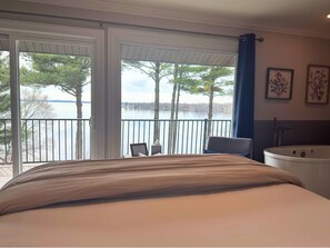 A bedroom with a bed, a chair, a bathtub, and a balcony with a view of trees and water. - Inn On Lake Wissota (Chippewa Falls)