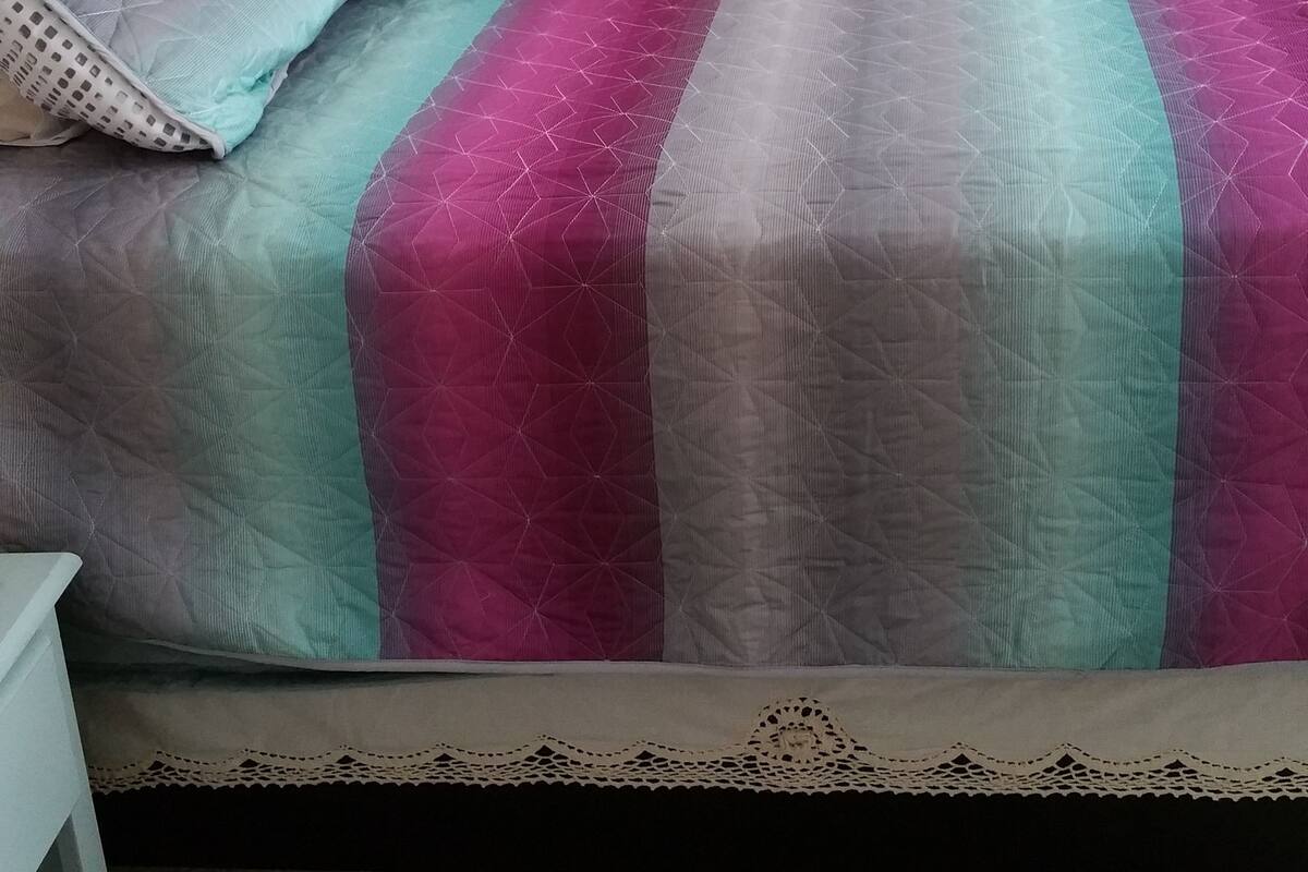 A bed with a striped bedspread, pillows, and a lace-trimmed headboard.
