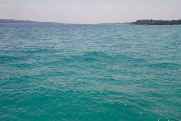 A calm sea with gentle waves, a distant shoreline with trees, and a small boat in the distance.