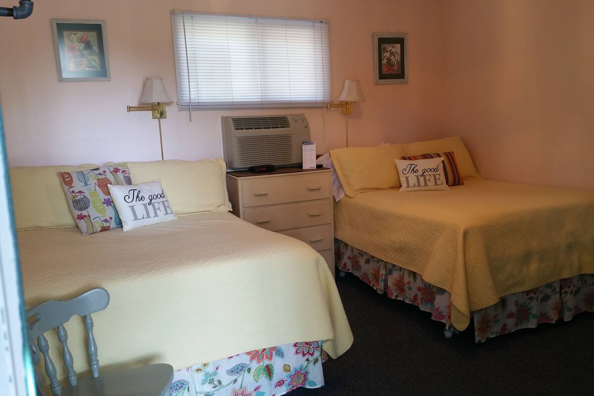 A bedroom with two beds, a nightstand, a heater, and two wall-mounted lamps.