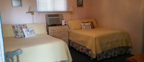 A bedroom with two beds, a nightstand, a heater, and two wall-mounted lamps.