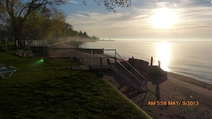 A beach with a wooden walkway and benches, a small wooden structure, and a clear sky with the sun low on the horizon.