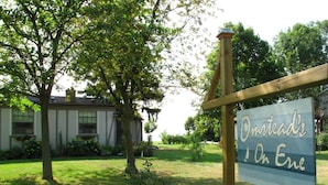 A sign for 'Oomstead's On Eric' in a grassy area with trees and a building in the background.