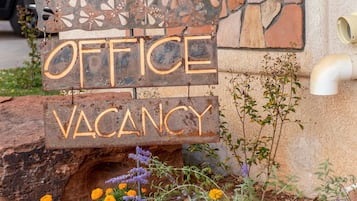 A wooden sign with "OFFICE VACANCY" written on it, placed in front of a building with a window and a planter with flowers.