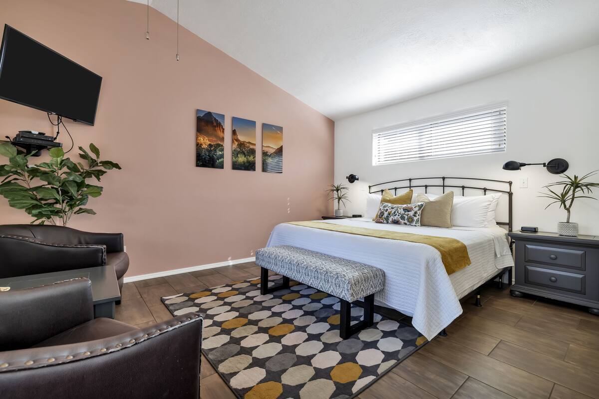A bedroom with a bed, bedside tables, a bench, a TV, and a plant.