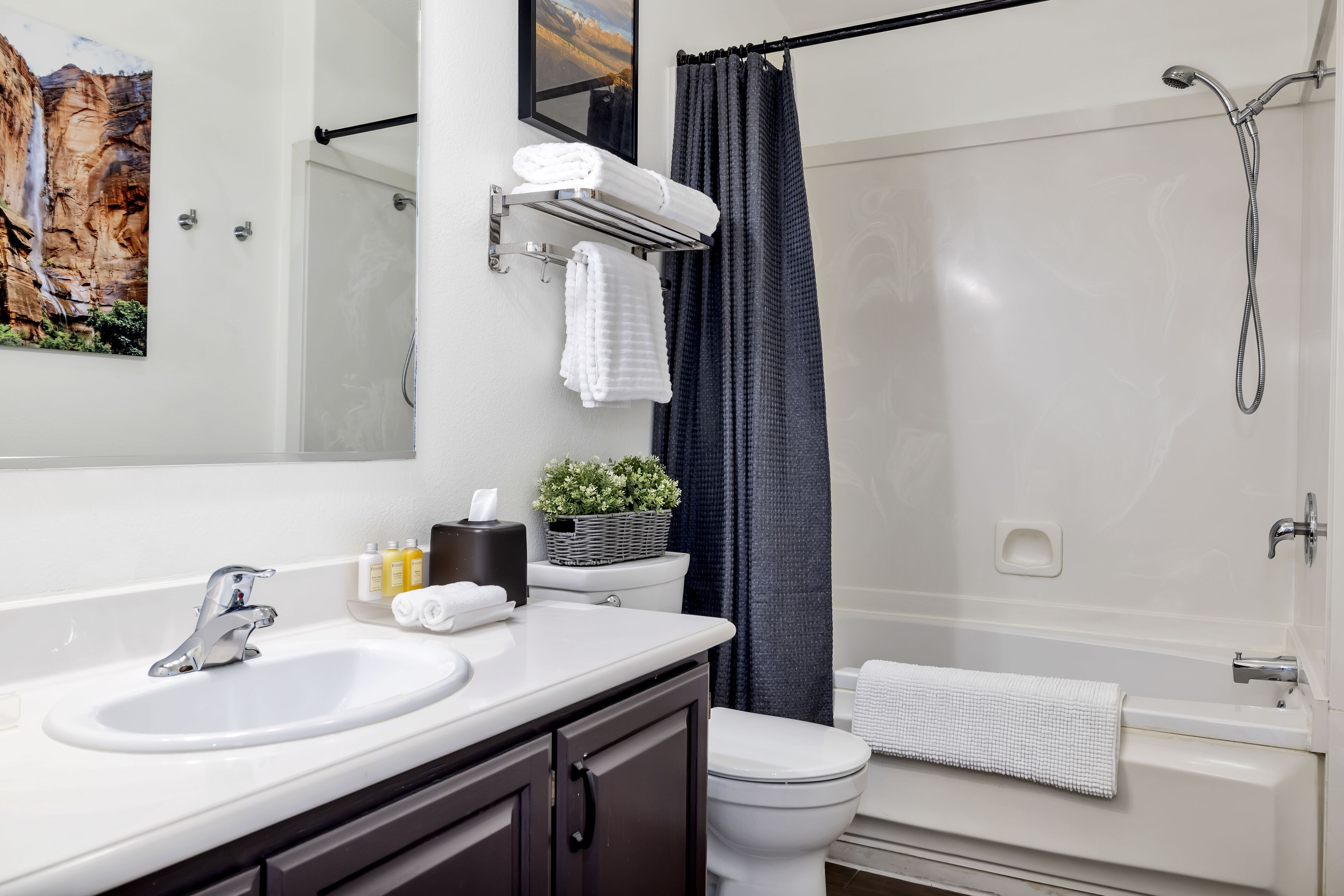 A modern bathroom with a white sink, dark cabinets, a toilet, a shower with a black curtain, and a framed picture on the wall.