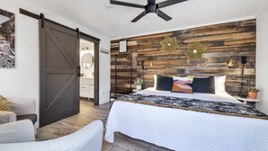 Un dormitorio con cama, ventilador de techo, cabecera de madera, mesita de noche y lámpara fijada a la pared.
