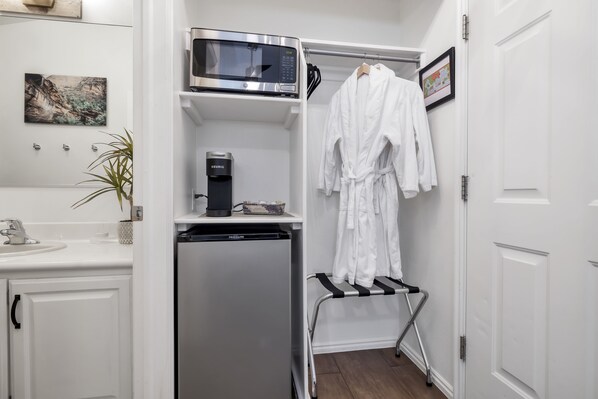 A compact bathroom with a white sink, a microwave, a coffee maker, and a drying rack with a robe.