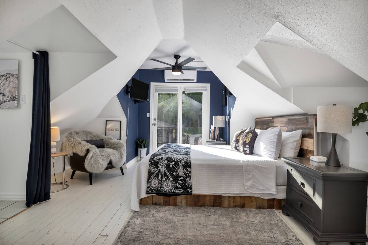 A bedroom with a sloped ceiling, a bed with a floral bedspread, a wooden nightstand, and a ceiling fan.