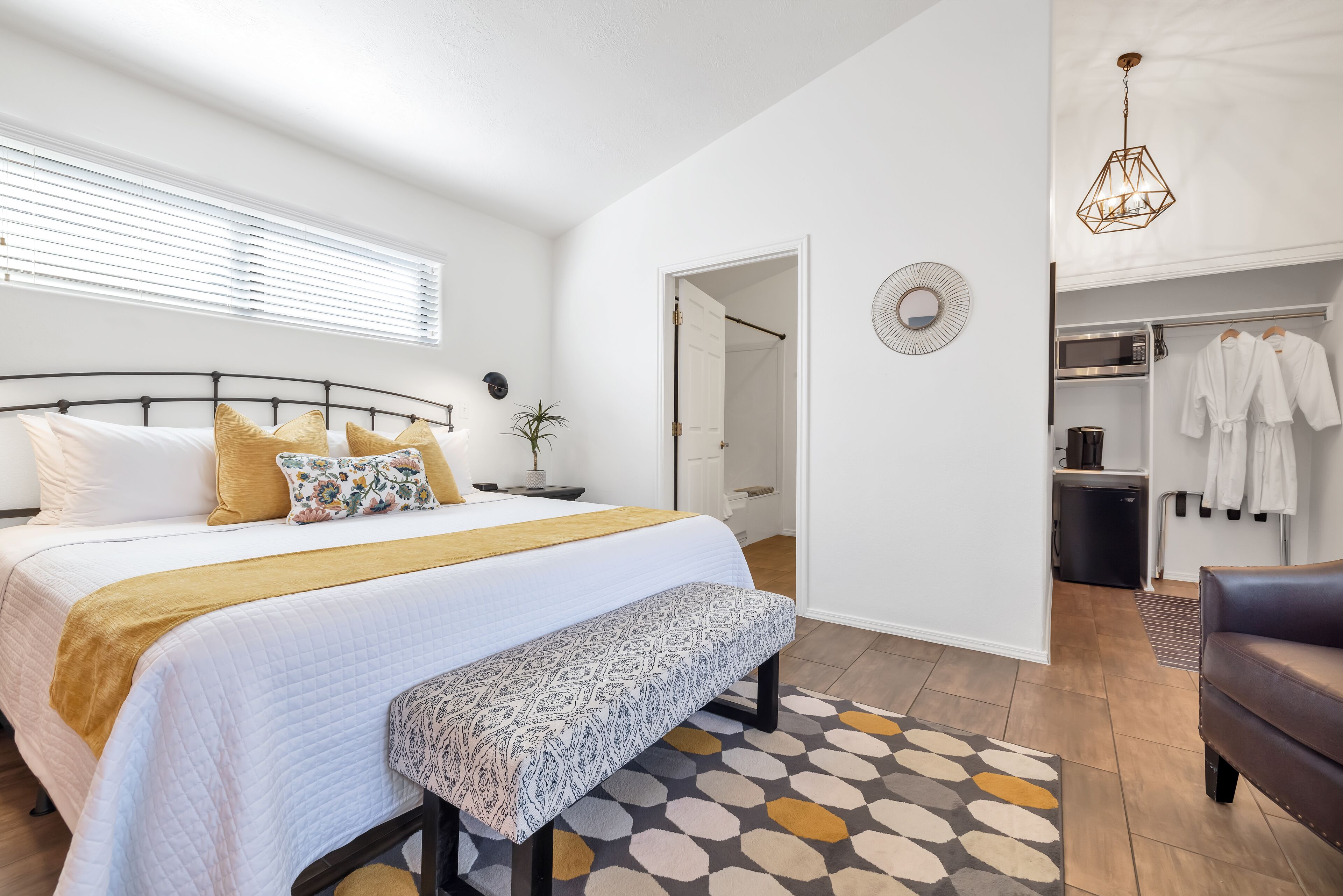 Une chambre à coucher comprenant un lit, une table de chevet, un banc et un dressing avec des vêtements suspendus.