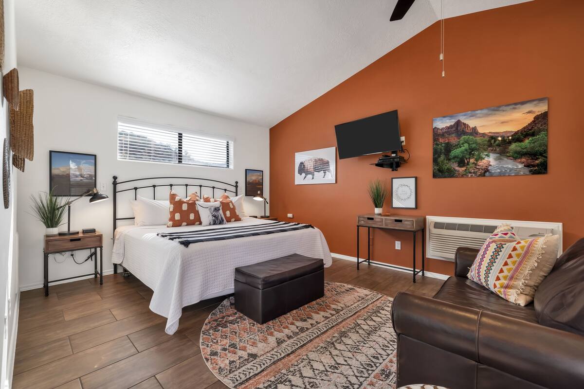 A bedroom with a bed, bedside tables, a TV, and a painting on the wall.