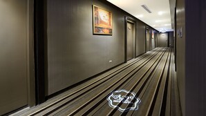 Un pasillo de hotel con alfombra a rayas, puertas y un cuadro en la pared.