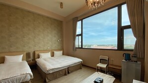 Habitación de hotel con dos camas, una mesita, una silla, una ventana con vistas y un candelabro.