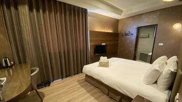 Habitación de hotel con cama, escritorio, silla, teléfono y televisor.
