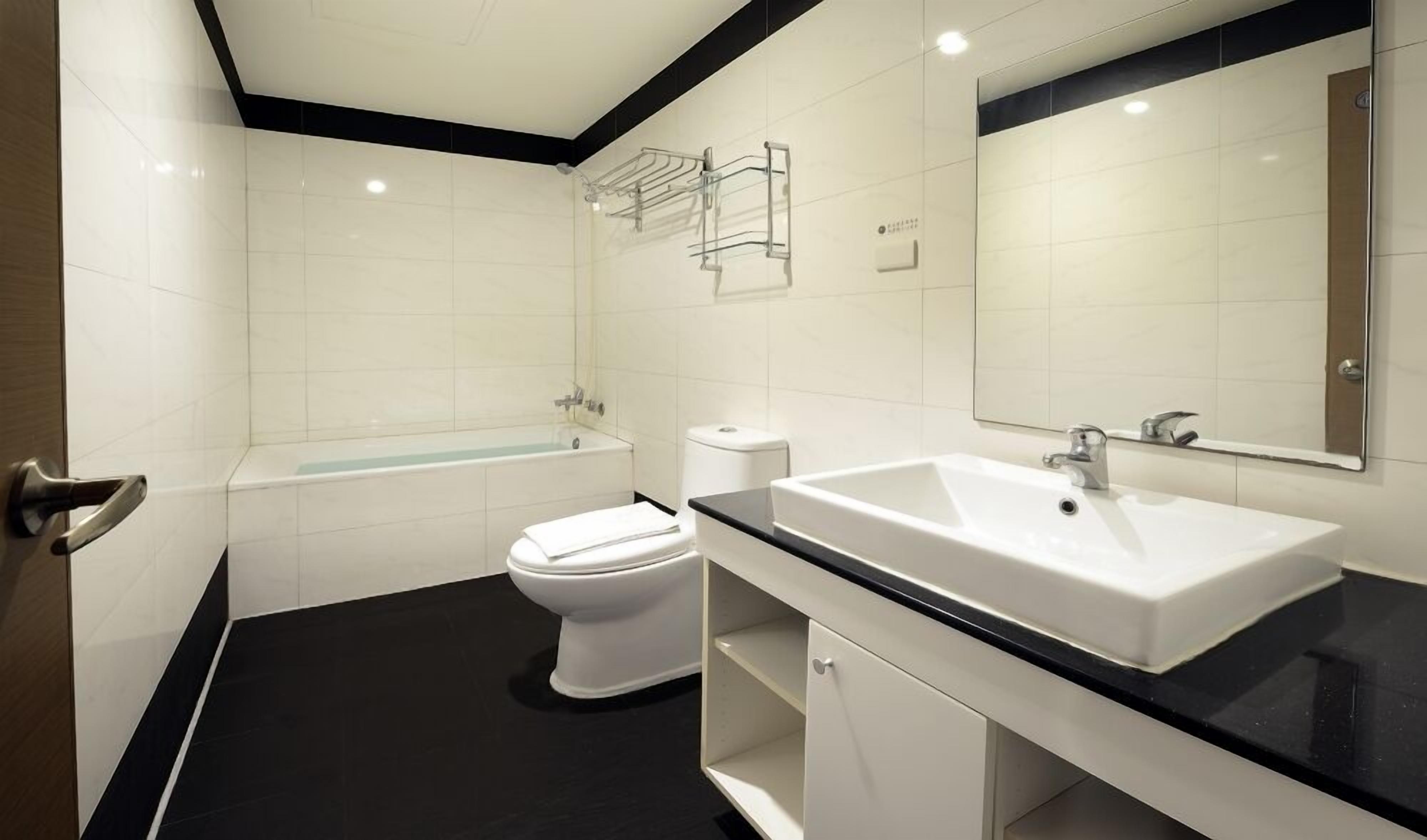 A modern bathroom with a white toilet, a bathtub, a sink, and a mirror.