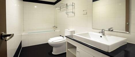 A modern bathroom with a white toilet, a bathtub, a sink, and a mirror.