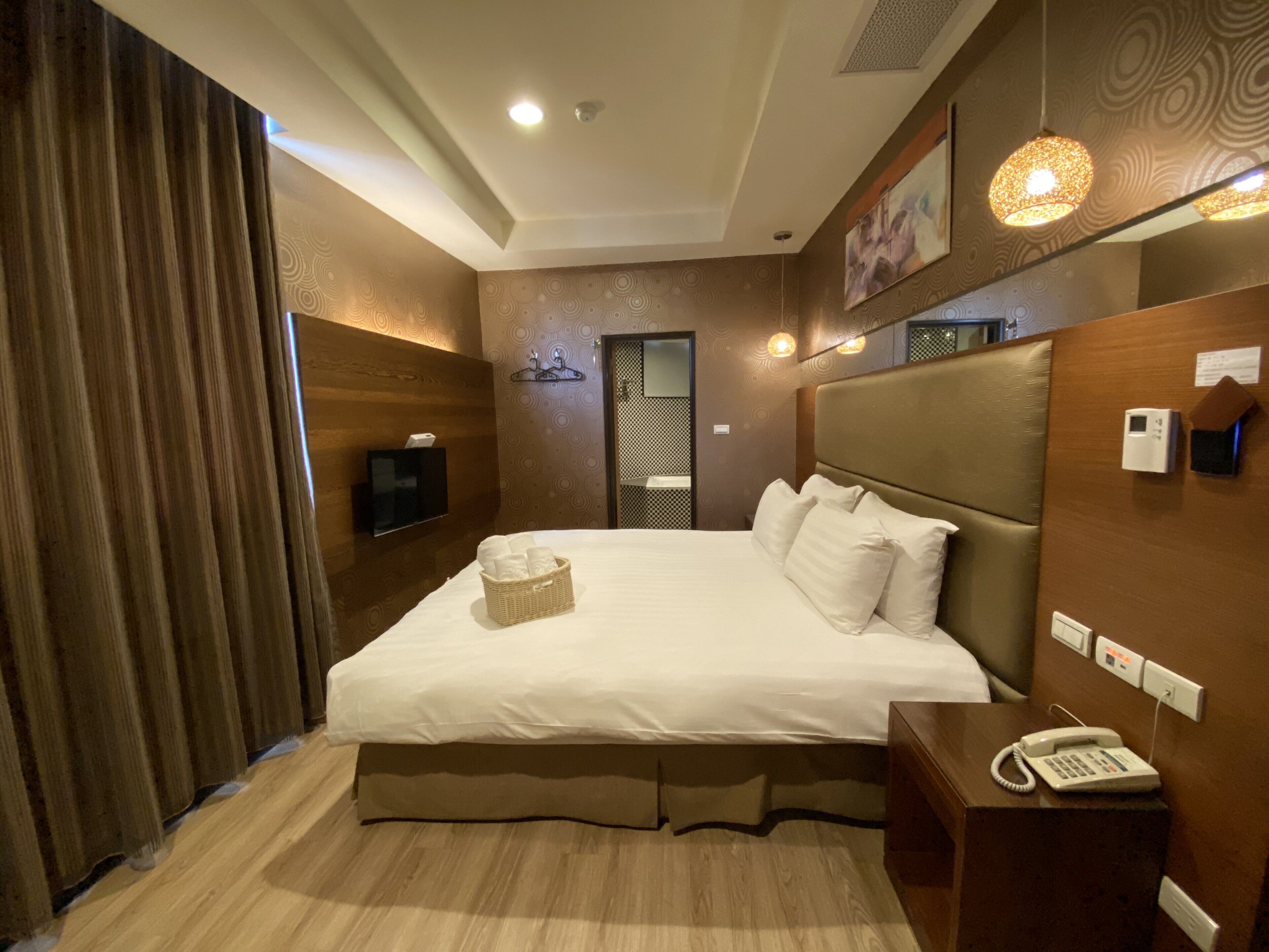 Habitación de hotel con una cama grande, una mesita de noche con teléfono, un televisor montado en la pared y un panel decorativo.