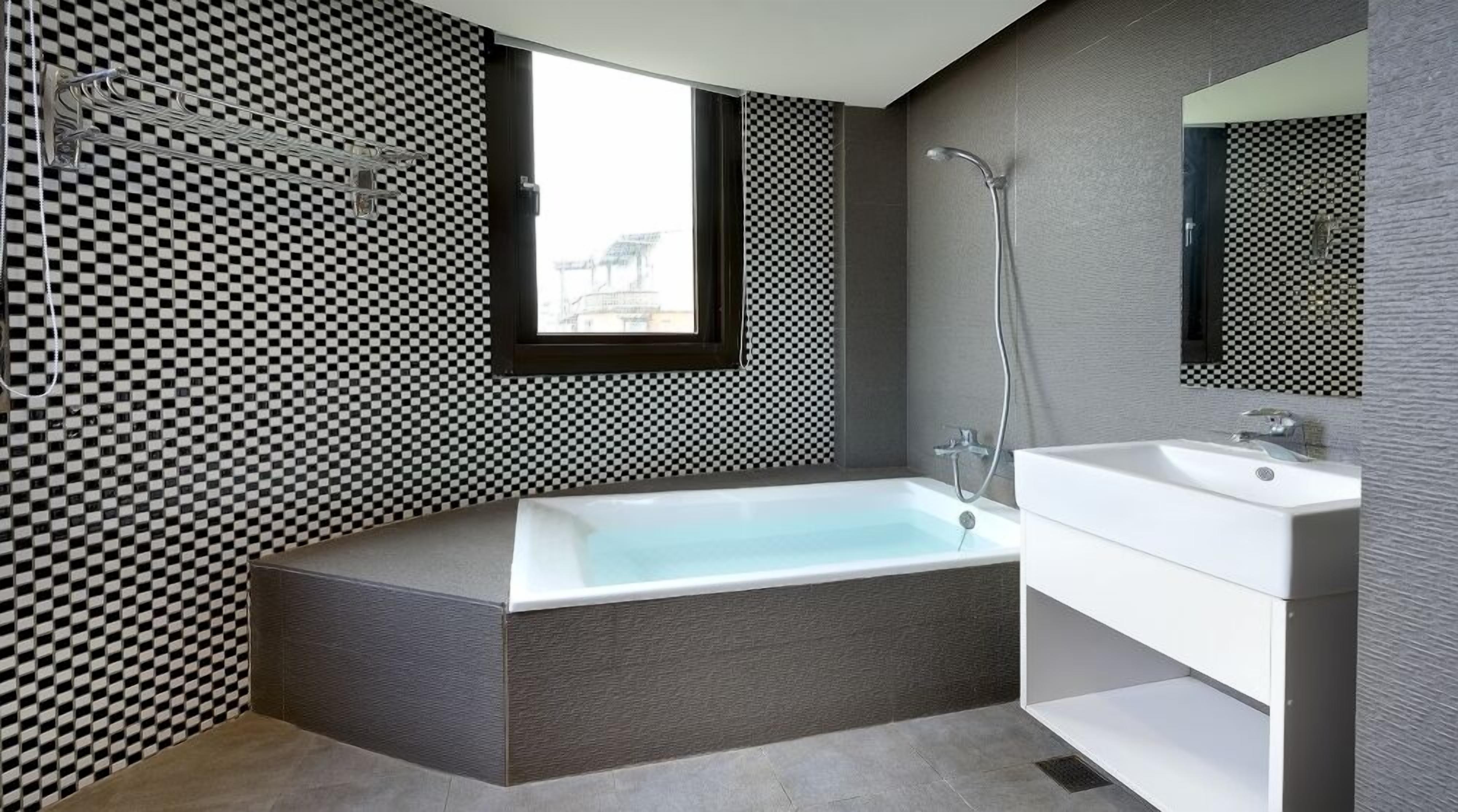 Une salle de bain moderne avec un motif à carreaux sur le mur, une grande baignoire, un lavabo blanc et un miroir.