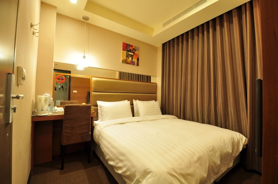 Habitación de hotel con cama, escritorio, silla, cafetera y un cuadro en la pared.