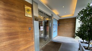 Entrada moderna de edificio con un muro de madera, puertas de cristal y una pequeña planta de interior.