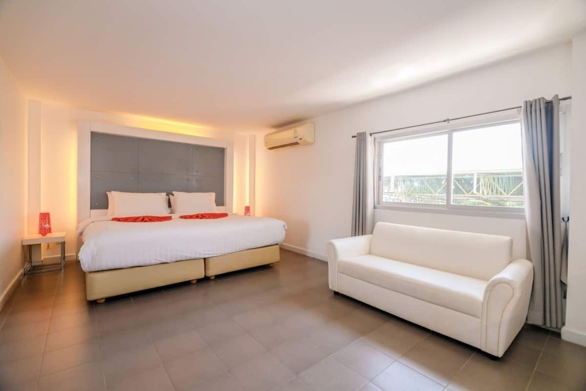 Una habitación de hotel moderna con una cama grande, un sofá, una mesita de noche y una ventana con cortinas.