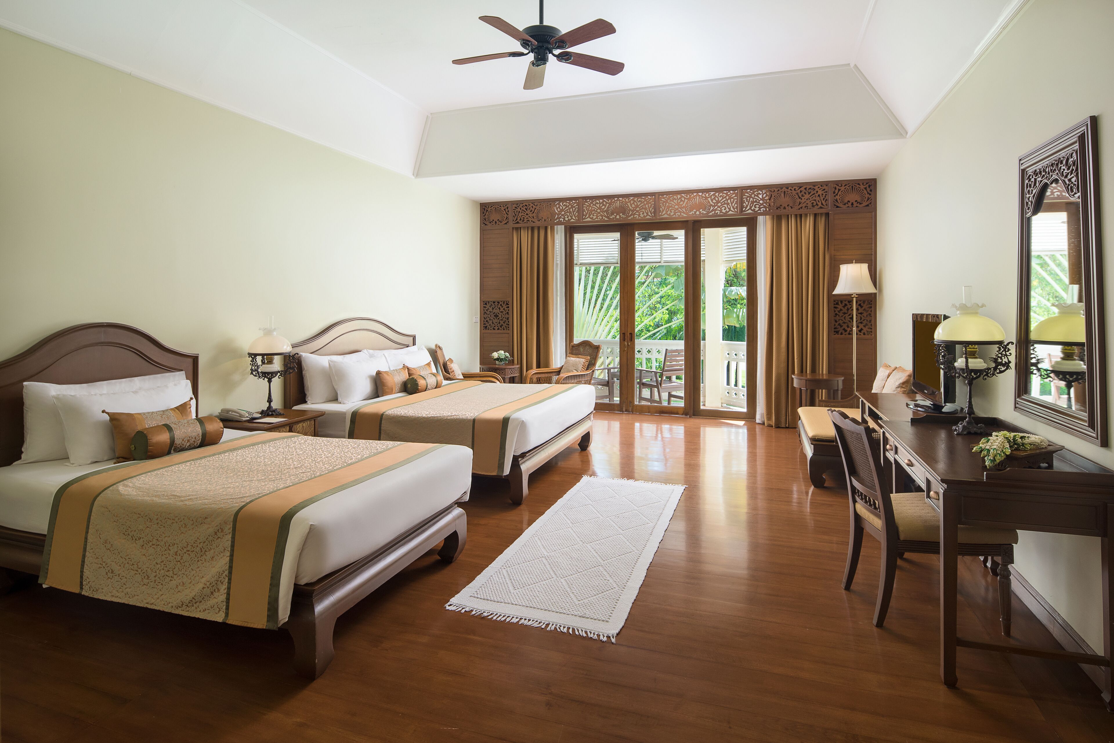 A hotel room with two beds, a desk, and a balcony with curtains.