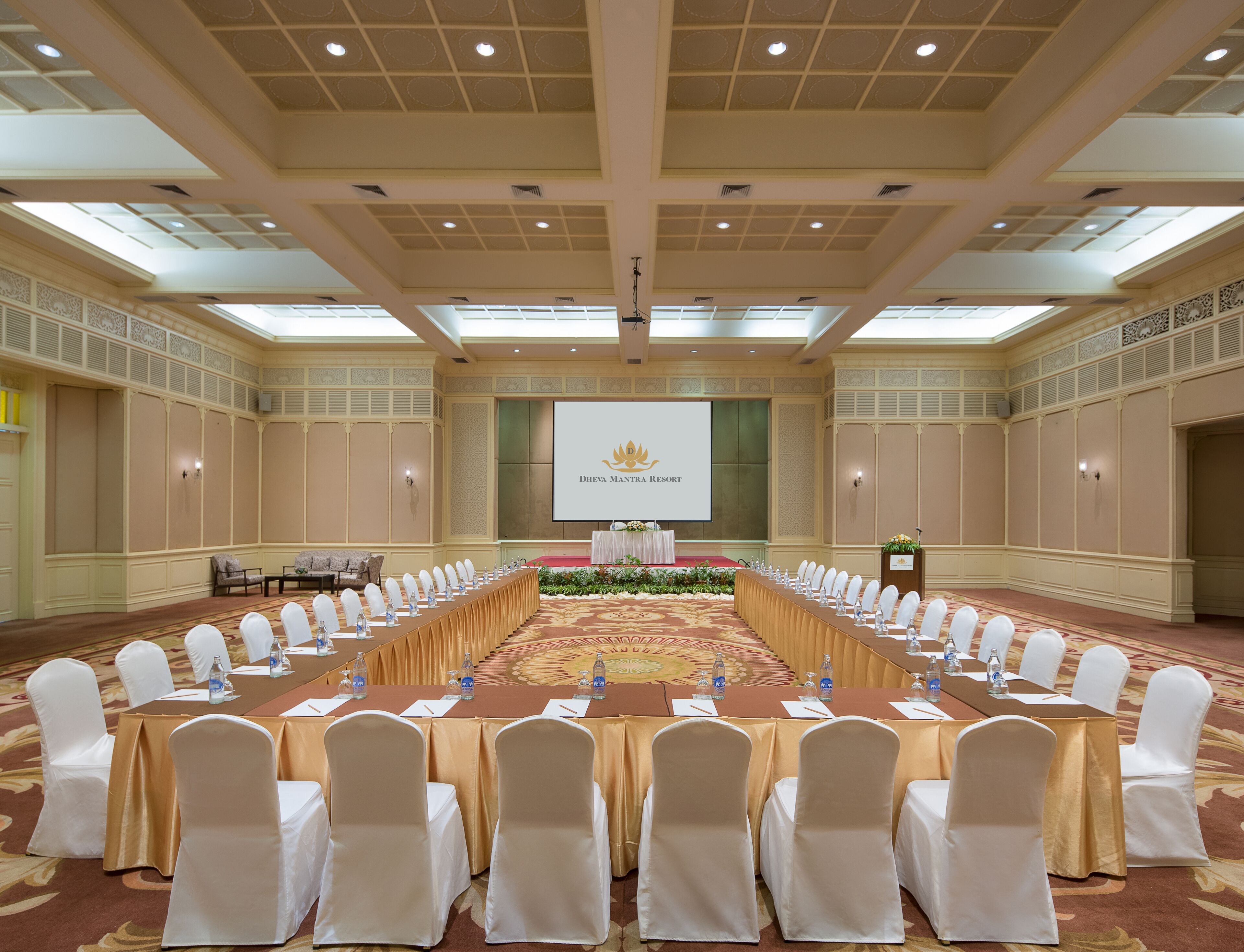 Un salón de conferencias con una larga mesa, sillas blancas y un atril.