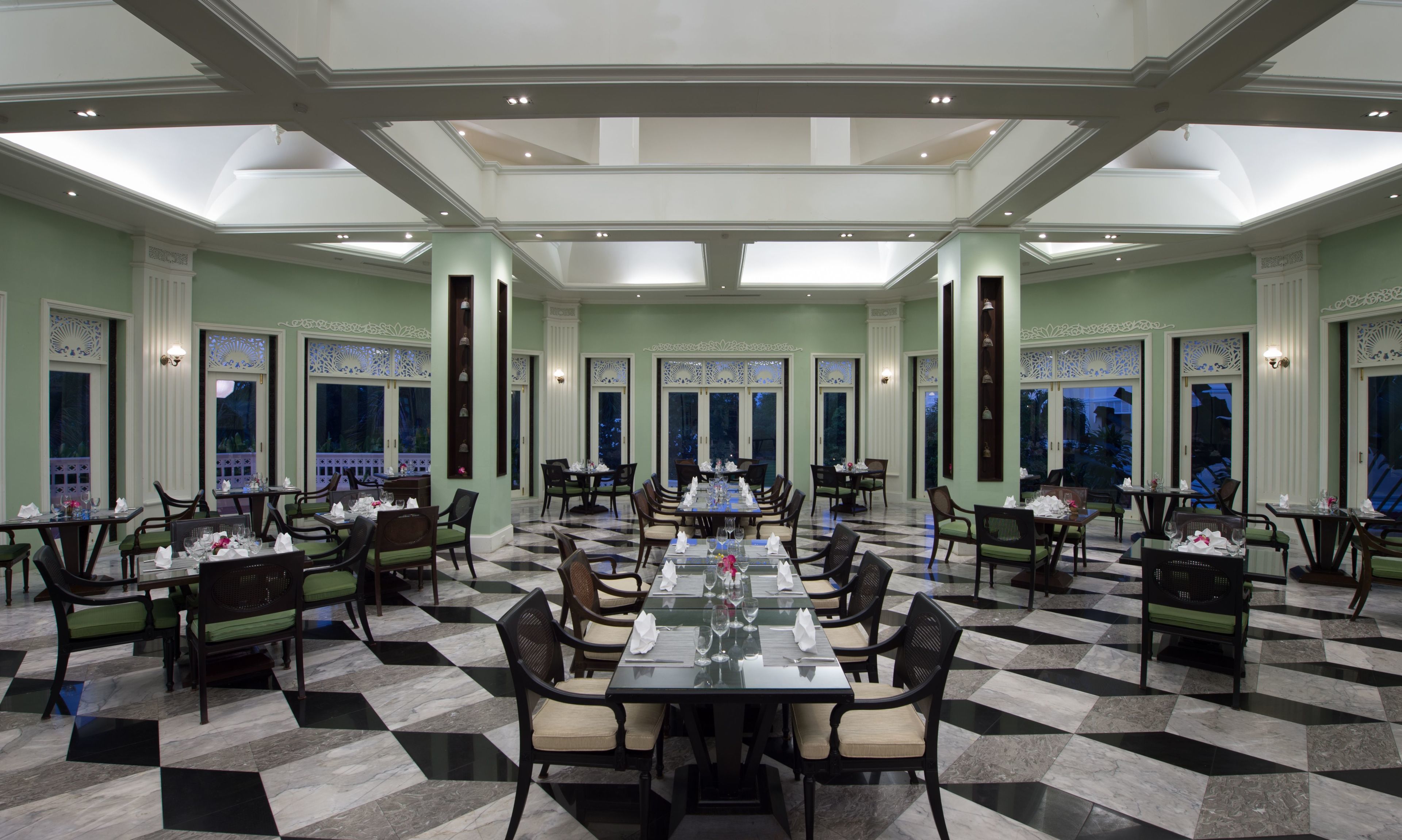 A spacious dining area with high ceilings and large windows, featuring a checkered floor and elegant table settings.