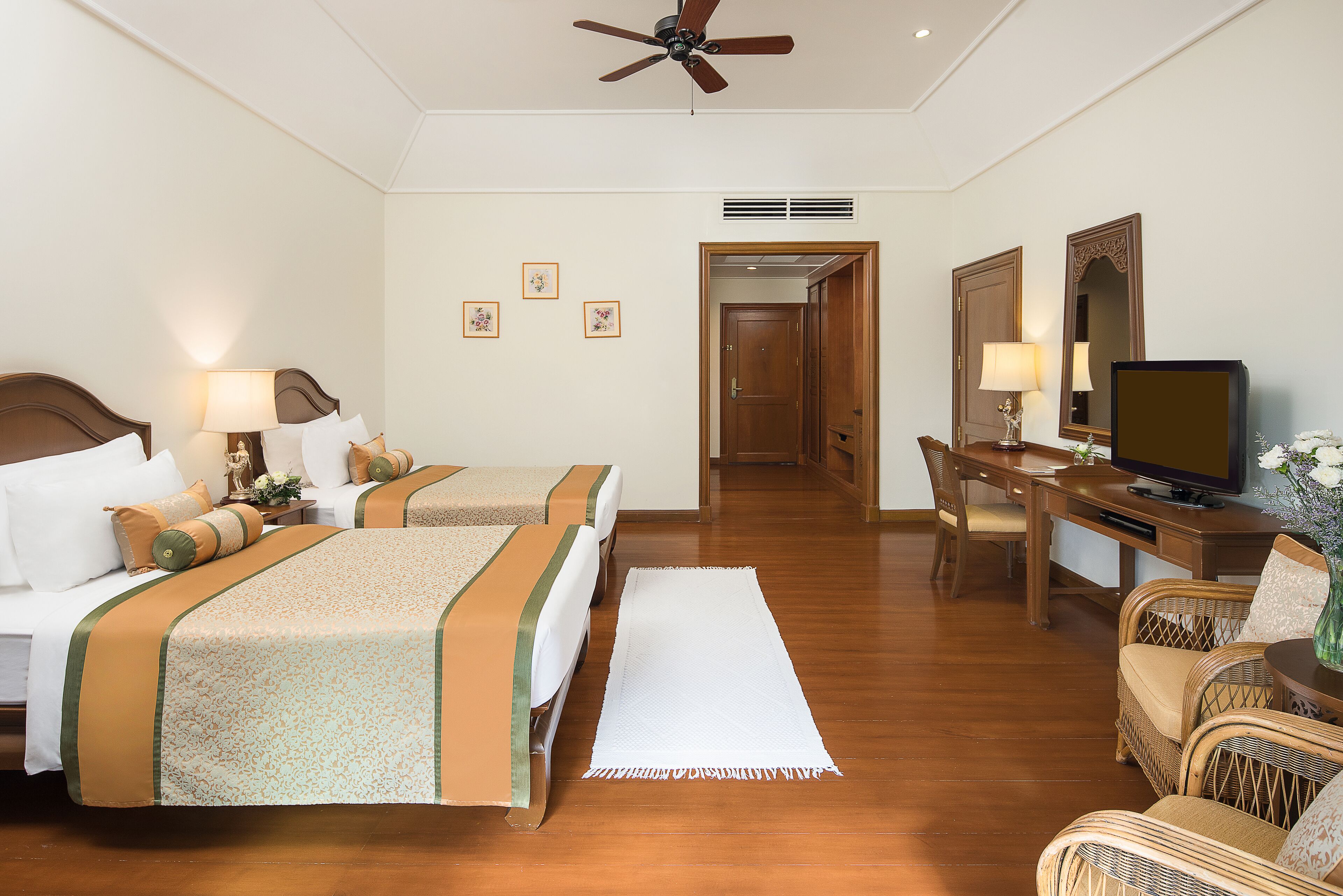 A hotel room with two beds, a desk, a television, and a ceiling fan.