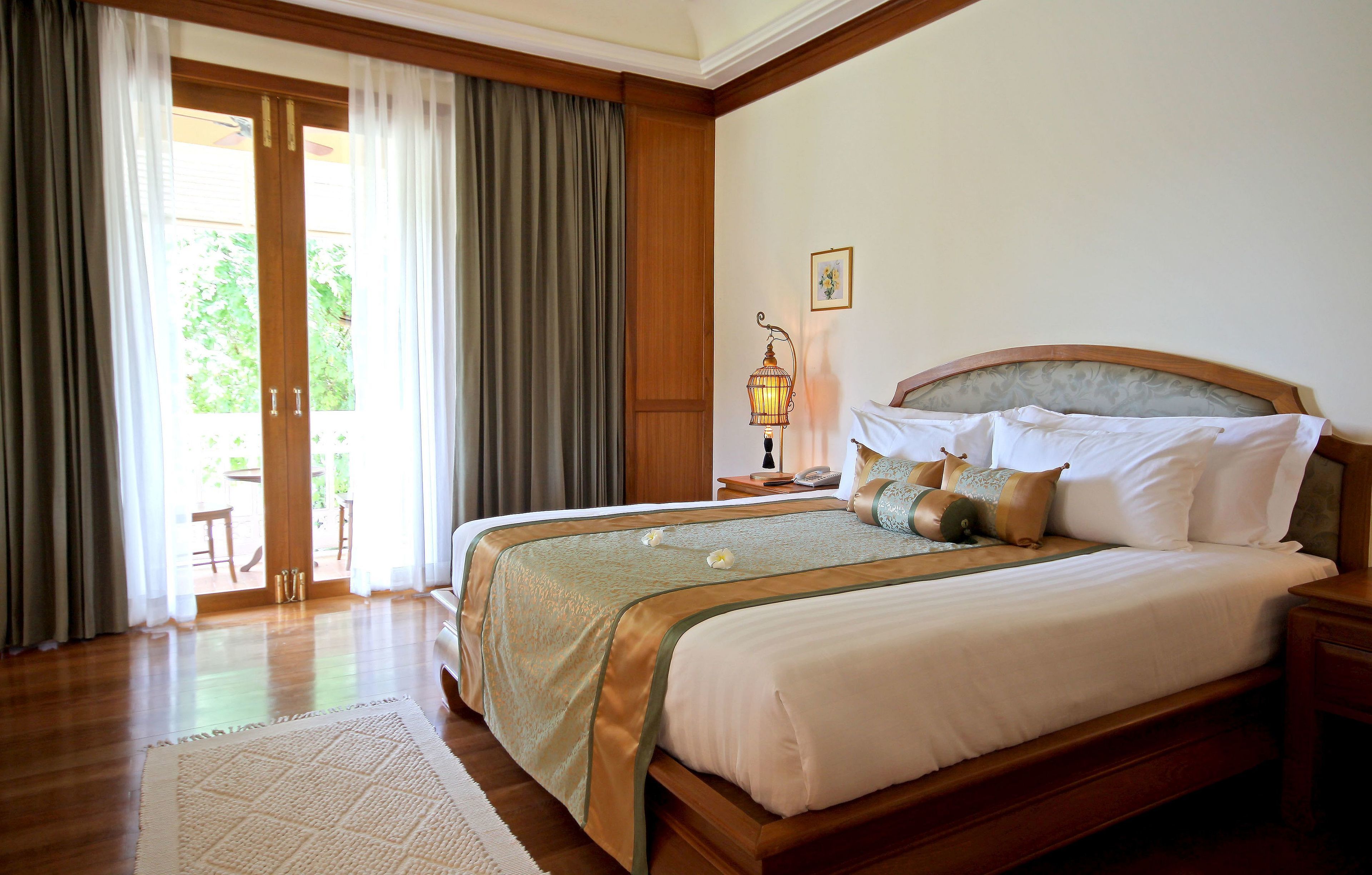 A large bed with a wooden headboard, a nightstand with a lamp, and a view of the outdoors through a sliding glass door.
