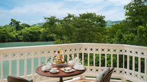 A balcony with a table set for tea service, overlooking a body of water and lush greenery.