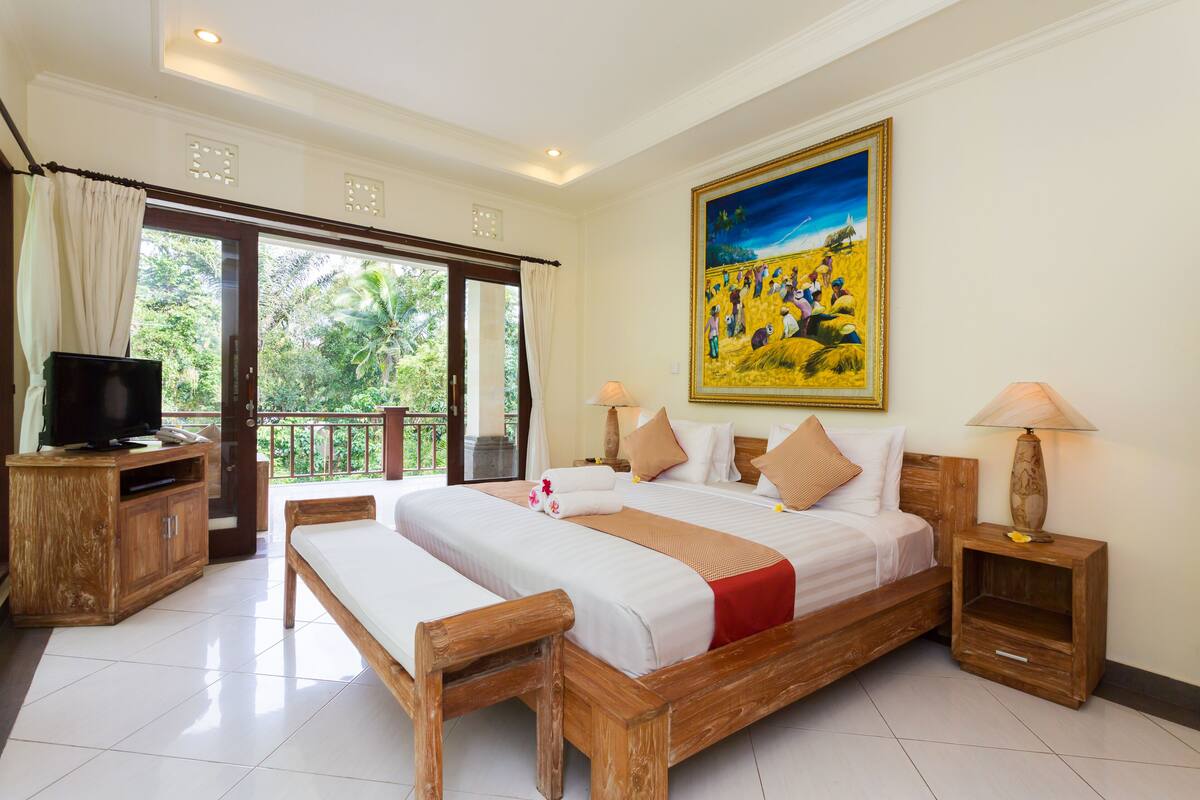 A spacious bedroom with a large bed, wooden headboard, and a balcony with curtains.