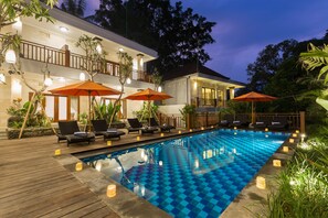 A swimming pool with lounge chairs and umbrellas, surrounded by a wooden deck and plants. - Puri Payogan Villa Ubud (Ubud)
