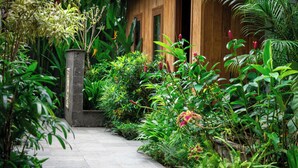 A wooden house with a stone pillar and a pathway surrounded by lush greenery and tropical plants. - Puri Payogan Villa Ubud (Ubud)