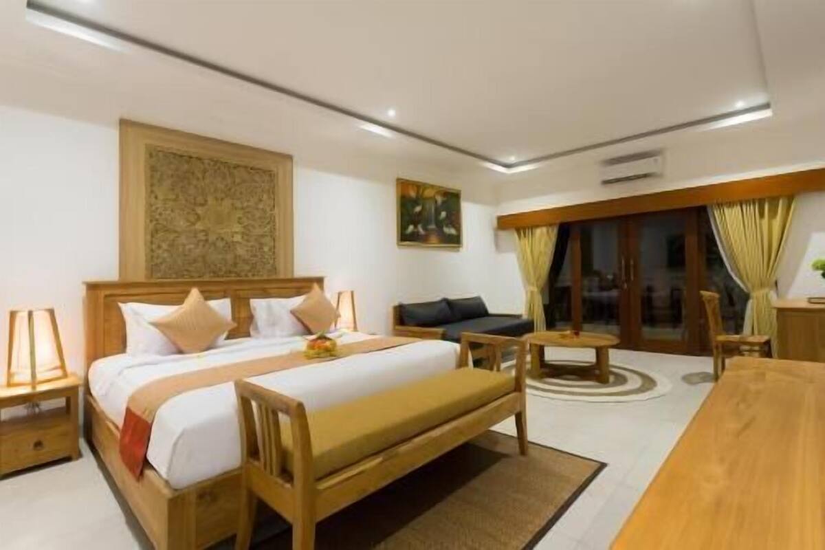 A hotel room with a bed, a sofa, a dining table, and a view of the outside.