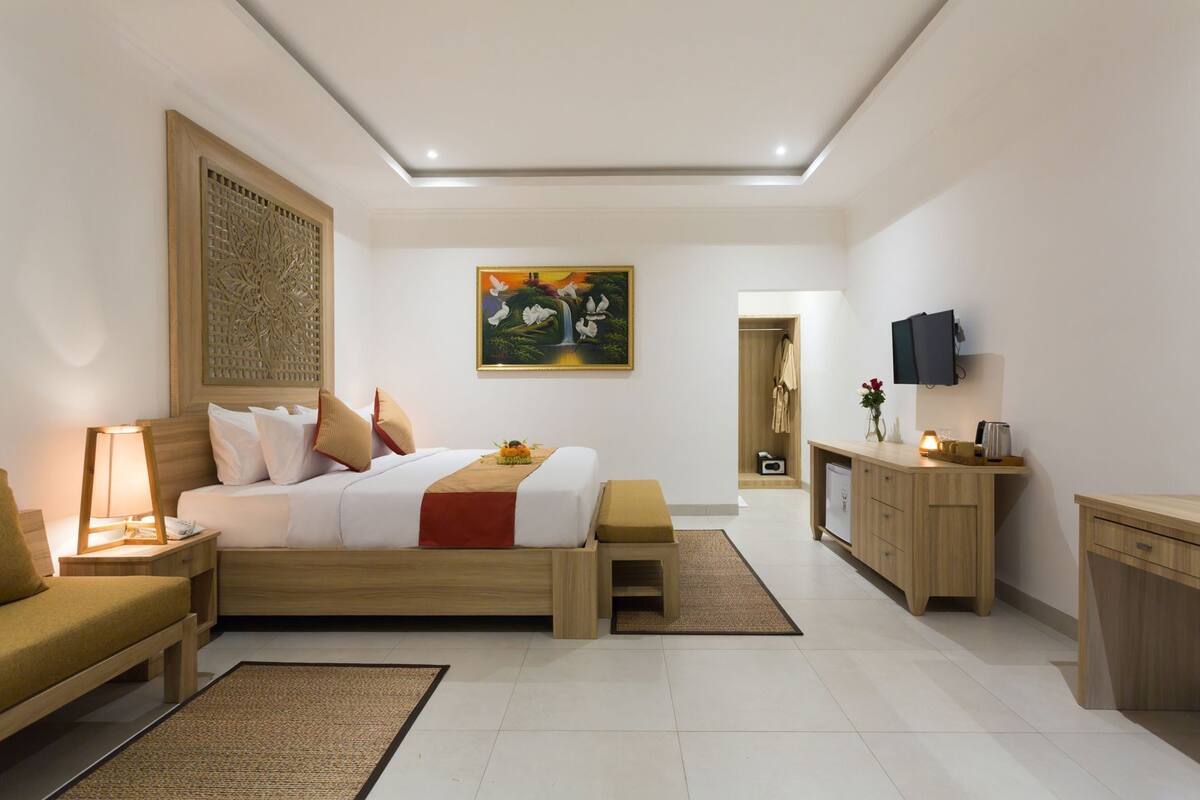 A modern hotel room with a bed, bedside table, lamp, wooden bench, and a desk with a TV.