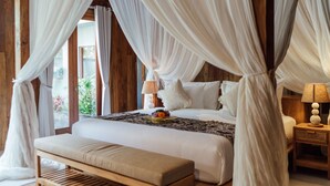 A bedroom with a canopy bed, wooden beams, a bench, and a bedside table with a lamp. - Puri Payogan Villa Ubud (Ubud)