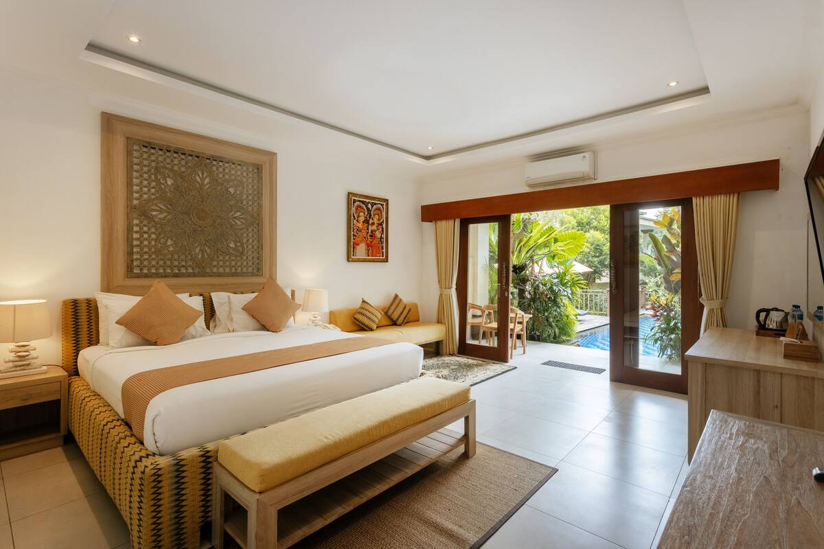 A modern hotel room with a large bed, a wooden bench, a desk, and a view of the outdoors.